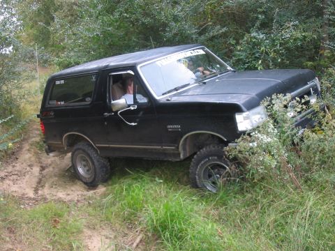 1988 Ford Bronco - Black Ford Bronco navigates an off-road trail with dense vegetation.
