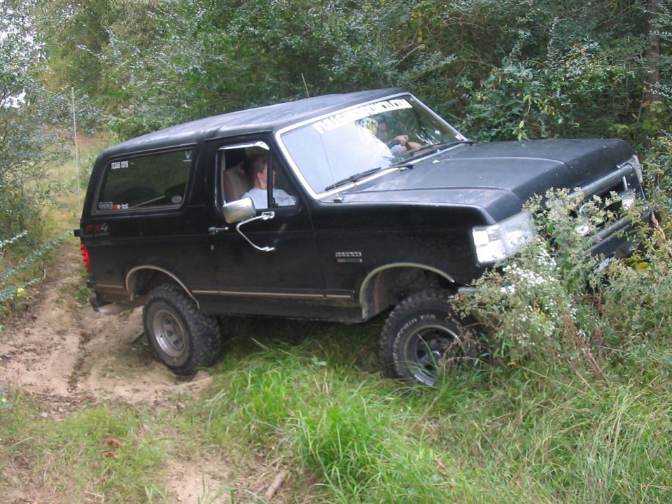 Black Ford Bronco driving off-road on a dirt path with grass and bushes