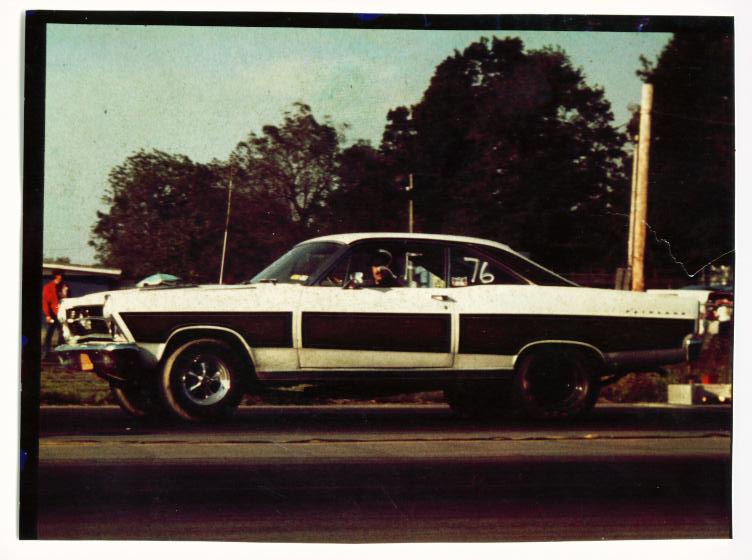 White vintage two-door coupe with '76' on rear window, side view, on pavement
