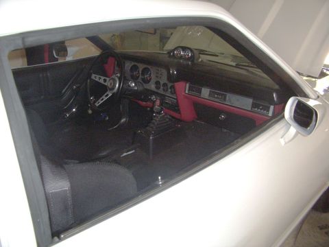 1978 Ford Mustang II - The interior of a white vehicle is visible, a black and red dashboard and a manual transmission shifter.
