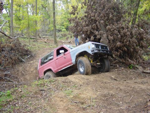 1983 Ford Bronco - Off-road SUV, possibly a 1983 Ford Bronco, navigates a steep, muddy incline in a wooded area.