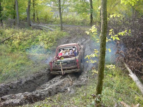 1983 Ford Bronco - Off-road adventure: A red pickup truck navigates a challenging muddy trail with passengers in the rear.
