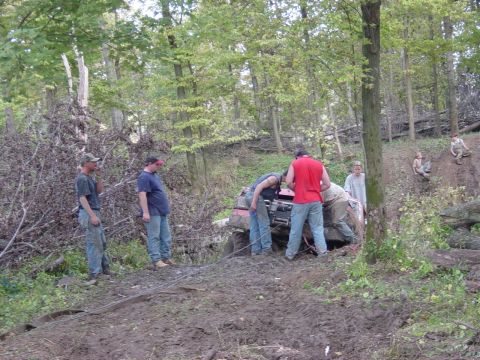 1983 Ford Bronco - A group of people are gathered around a red off-road vehicle that is stuck in the mud.