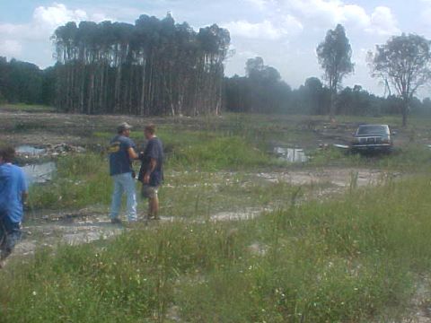 1992 Ford Bronco - A 1992 Ford Bronco is parked in a muddy, wooded area with two people standing nearby.