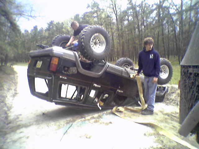 SUV flipped on its side with two guys nearby, one on top, one holding a strap