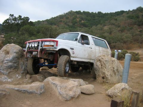 1985 Ford Bronco - A white SUV is shown navigating a challenging rocky obstacle course.
