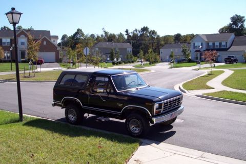 1983 Ford Bronco - A black Ford Bronco is parked on the side of a residential street on a sunny day.
