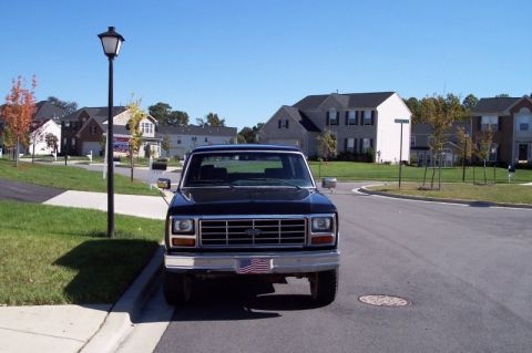 1983 Ford Bronco - A black Ford truck is parked on a suburban street in front of houses.