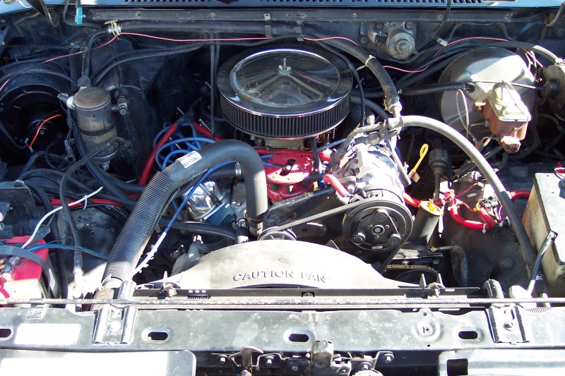 Engine bay with V8 engine, air cleaner, and various hoses and wires. 'CAUTION FAN' text visible on fan shroud