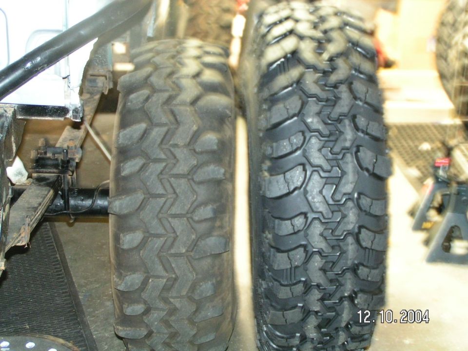 Two mud tires side by side under a vehicle on a shop floor with a date stamp of 12/10/2004
