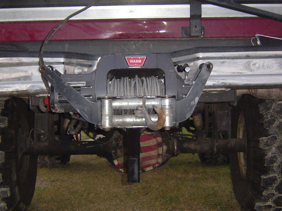 Rear view of a vehicle showing a Warn winch mounted on the bumper, with the rear axle and large tires visible