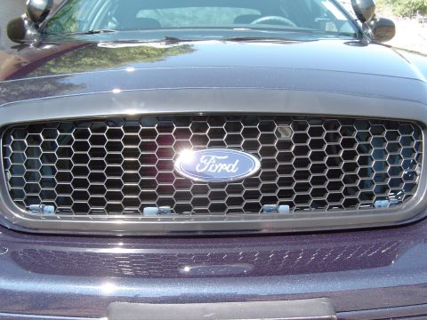 1999 Ford Crown Victoria - Close-up of the Ford emblem and aftermarket honeycomb grille on a dark-colored vehicle, possibly a police car.