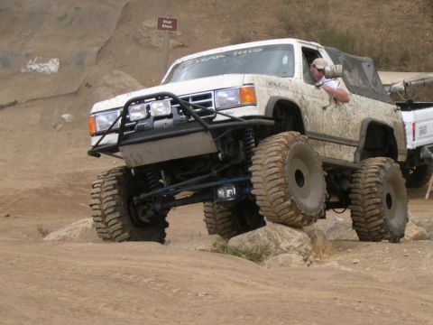 1990 Ford Bronco - Modified off-road truck navigates rocky terrain with a driver behind the wheel.