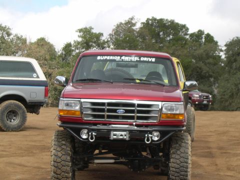 1990 Ford Bronco - Modified red Ford Bronco with aftermarket bumper and winch, parked outdoors with other vehicles.