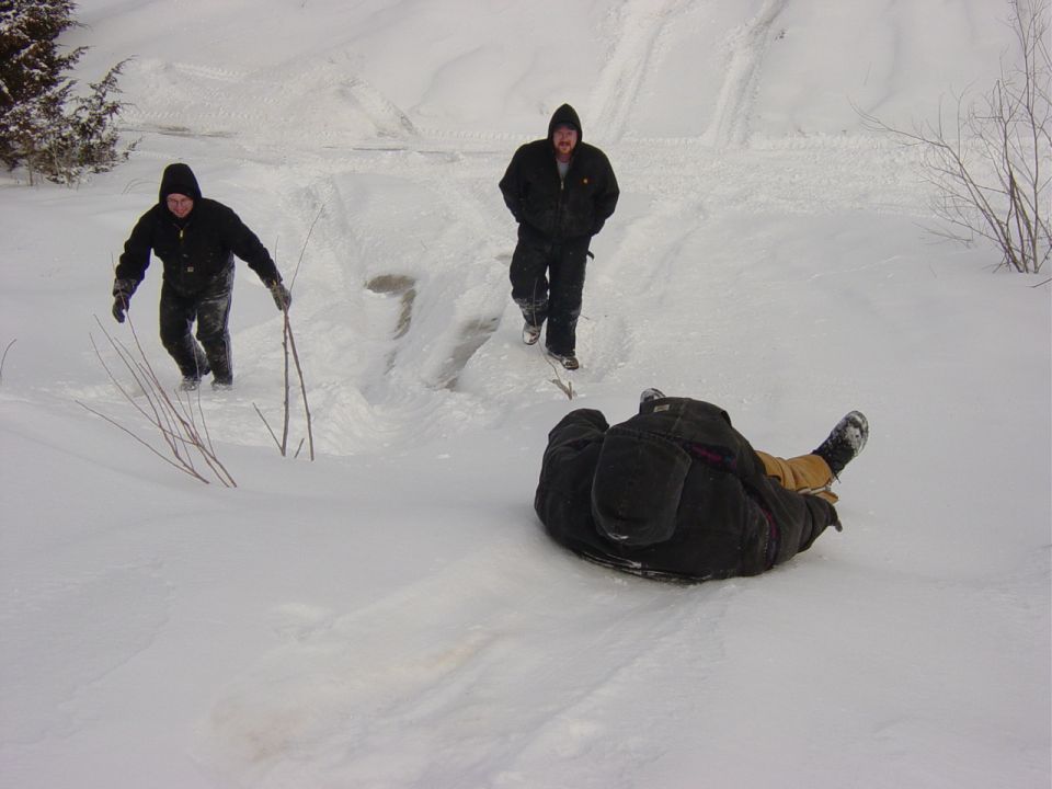Three people in winter coveralls sledding and hiking on a deep snowy hillside
