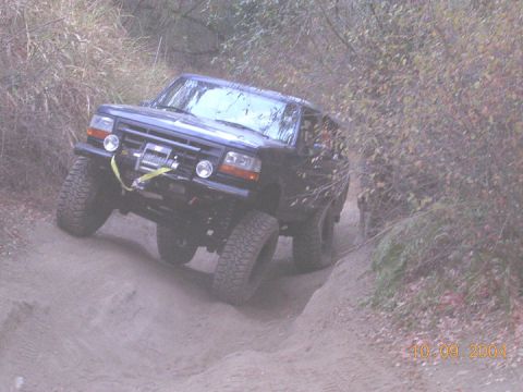 1994 Ford Bronco - A black Ford Bronco navigates a steep, sandy incline surrounded by foliage.
