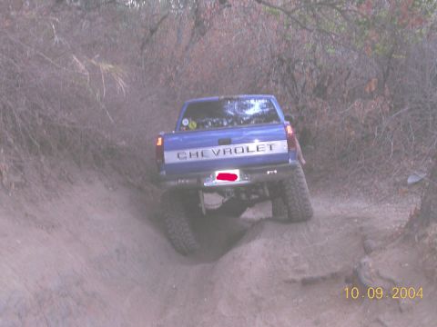 1994 Ford Bronco - A blue Chevrolet pickup truck navigates a challenging off-road trail, kicking up dust as it goes.