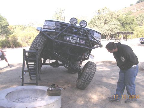1994 Ford Bronco - A heavily modified 1994 Ford Bronco with a custom roll cage and winch is displayed at an angle, with a person observing it.