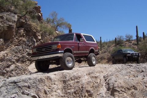 1992 Ford Bronco - A maroon Ford Bronco navigates a rocky desert trail with another vehicle in the background.
