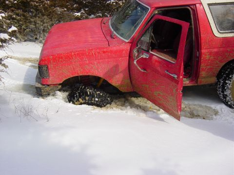 1983 Ford Bronco - A red 1983 Ford Bronco is stuck in the snow, its driver's door ajar.
