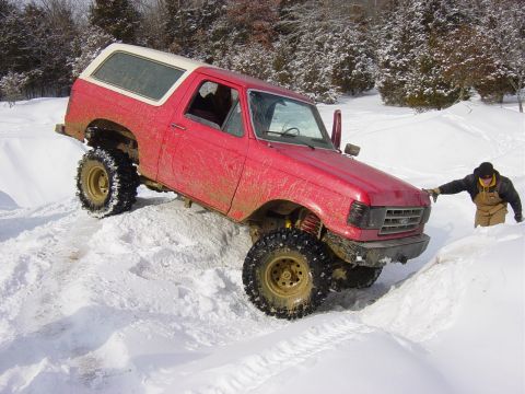 1983 Ford Bronco - A red Ford Bronco navigates a snowy terrain with a person assisting.