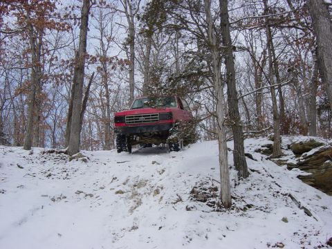 1983 Ford Bronco - This red SUV navigates a snowy incline amidst bare trees, its grille suggesting an early 1980s model.