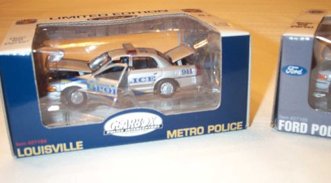 1998 Ford Crown Victoria - A close-up of a toy police car in its packaging, with another toy car box visible to the right.