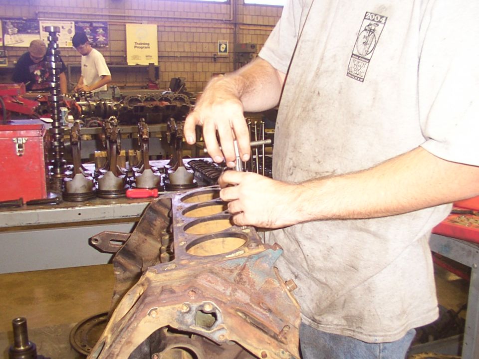 Mechanic working on engine block with pistons and camshaft laid out on table