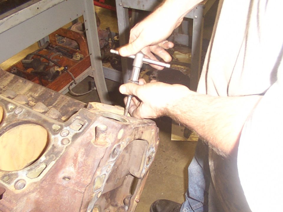 Hands using a tap handle to thread a hole in an engine block
