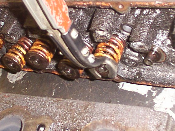 Hand tool positioned on rocker arm over rusty valve springs, valve cover off