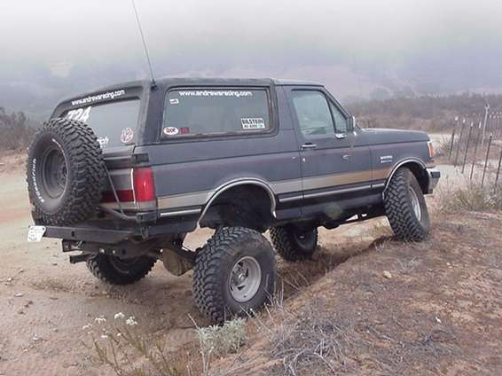 Rear quarter of a lifted dark Ford Bronco with rear spare on a foggy dirt trail