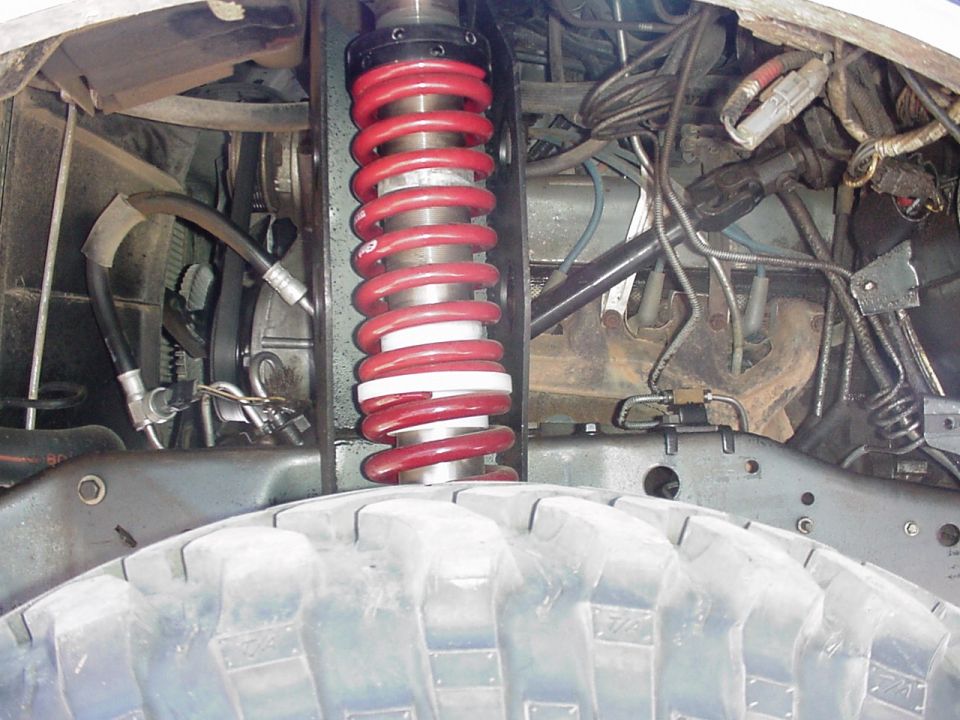 Close-up of a red coilover spring shock in a wheel well above a knobby tire