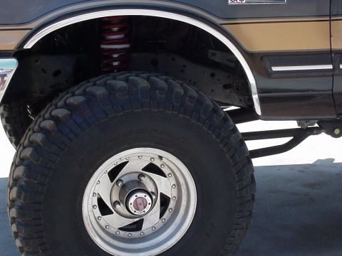 1990 Ford Bronco - front wheel of a lifted tan-and-brown truck with chrome wheel-well trim, an aluminum alloy wheel and a chunky mud-terrain tire.