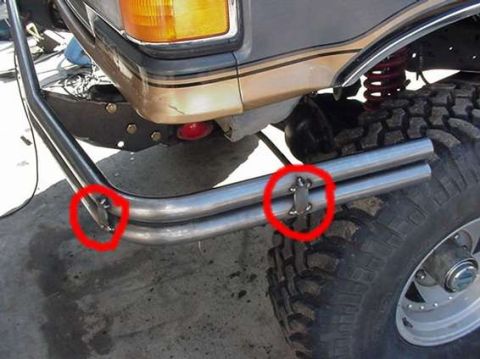 1990 Ford Bronco - Two red-circled mounting tabs on a polished tubular bumper meet the front fender of a lifted SUV with a coil-over shock and mud tire.