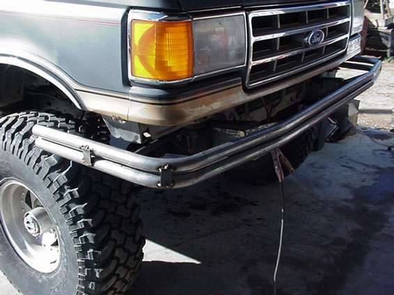 Bare-steel tube bumper bolted under the front of a gray-and-tan lifted Ford truck