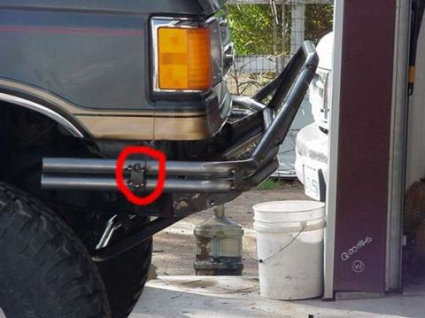 1990 Ford Bronco - red circle highlights a mounting bracket on the bare-steel tube bumper of a lifted Ford truck parked near a garage door.