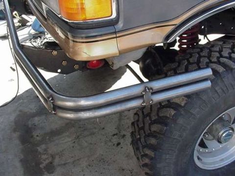 1990 Ford Bronco - Close view of polished tubular bumper tubes and mounting tabs at the front corner of a lifted SUV riding on a mud-terrain tire.