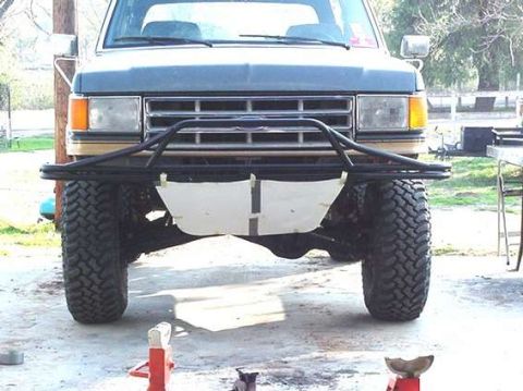 1990 Ford Bronco - Front view of a lifted Ford truck on a concrete floor with a tubular bumper, a white skid plate, and jack stands set out in front.