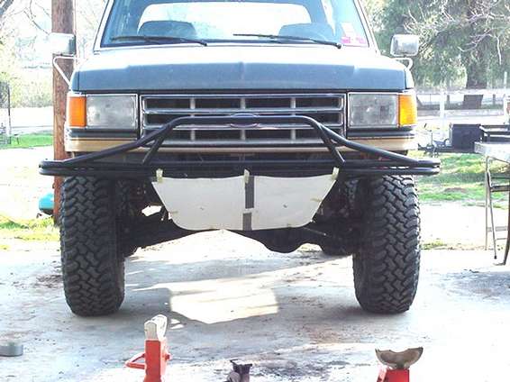 Front view of a lifted Ford truck with a tube bumper and white skid plate, jack stands on the floor