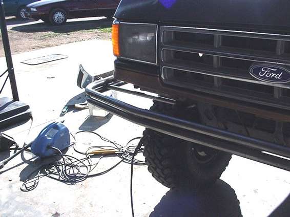 Black tube bumper on a lifted truck with Ford grille emblem, welding gear on the ground