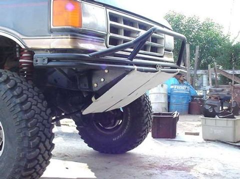 1990 Ford Bronco - Custom black tubular front bumper and skid plate beneath the front of a lifted Ford in a yard.
