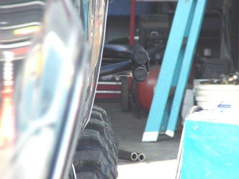 1990 Ford Bronco - Close-up of a black suspension link and oversized tire beside a vehicle body inside a workshop.