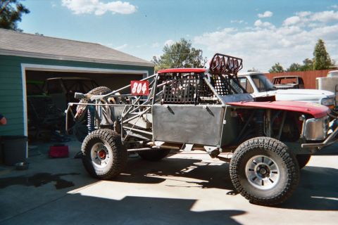 1990 Ford Bronco - tube-chassis off-road race truck marked 804 with red panels sits in a driveway by a garage.