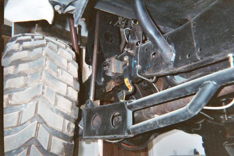 1990 Ford Bronco - Undercarriage view showing black frame, suspension links, wiring, and an off-road tire.