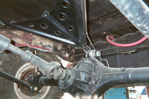1990 Ford Bronco - Underbody view of a rear axle, driveshaft, and triangulated suspension links with a red brake line.