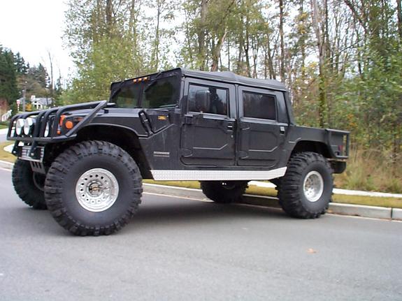 Black Hummer H1 four-door pickup truck with large off-road tires parked on a street