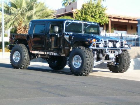1982 Ford Bronco - A modified black Hummer H1 pickup truck with oversized tires is seen from a three-quarter front angle on a sunny day.
