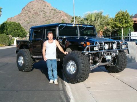 1982 Ford Bronco - A man poses with a black Hummer H1, oversized tires and a prominent chrome grille, under a clear sky.