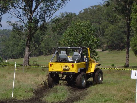 1982 Ford Bronco - A yellow off-road vehicle navigates a muddy course during an event.