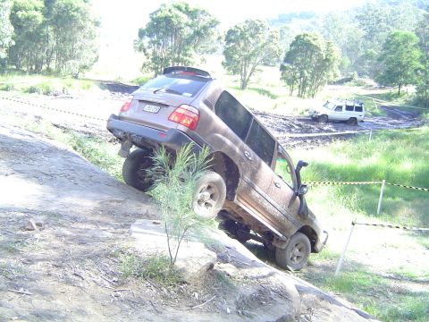 1982 Ford Bronco - Off-road vehicles navigate a challenging dirt course with steep ascents and muddy terrain.
